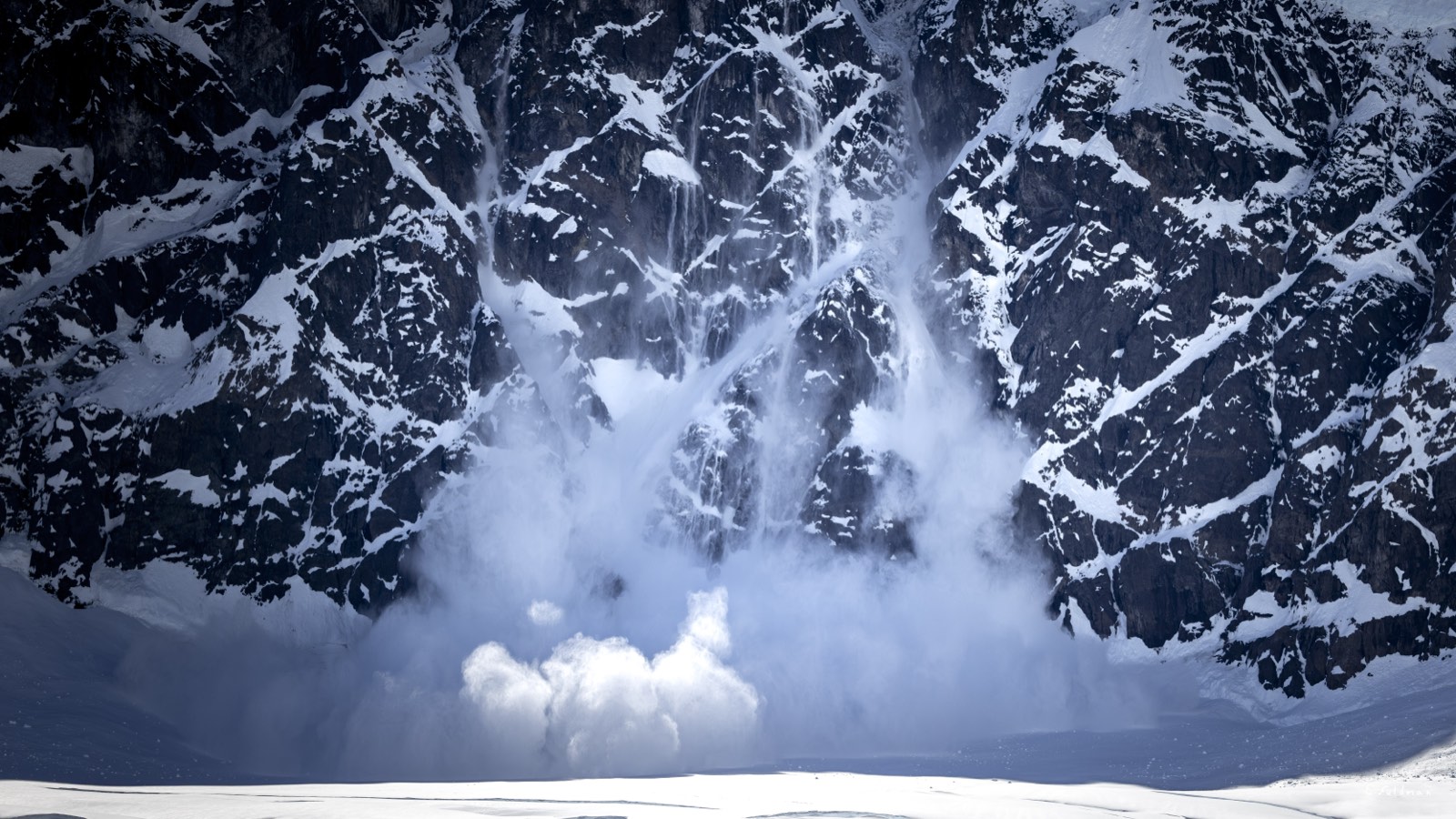 An avalanche falling down a dark mountain face
