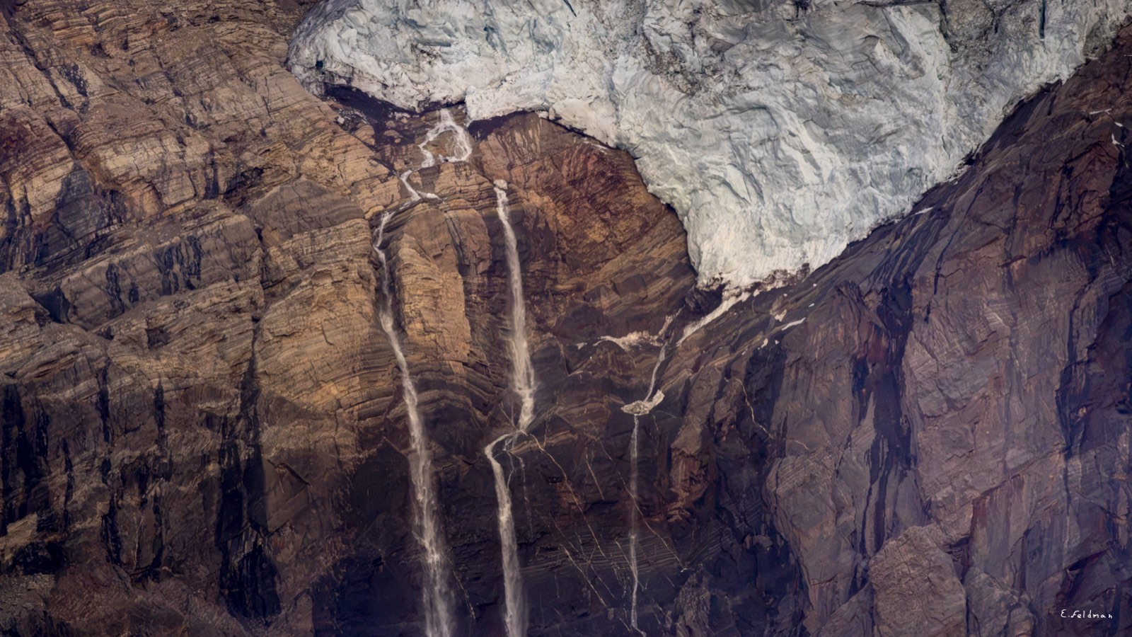 Waterfalls from a hanging glacier over layered cliffs